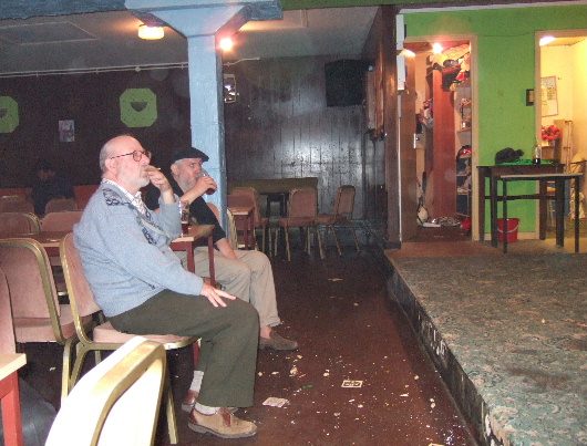 Two older gentlemen sat at the front in anotherwise deseted club.